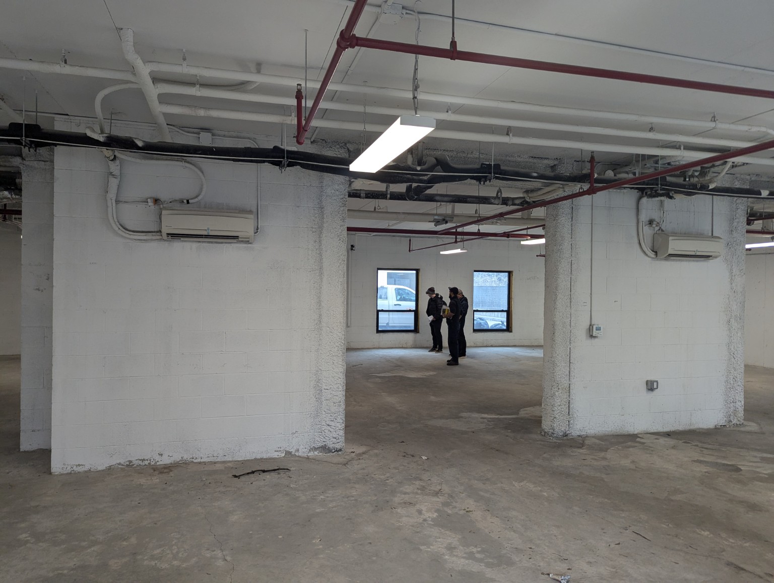 The current unfinished main space, with exposed ceiling pipes, wide white columns, and an opening to a room with windows
